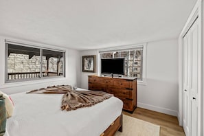 A bedroom with a bed, dresser, TV, and windows with stone walls.