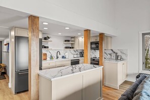 A modern kitchen with marble countertops, wooden beams, and a central island.