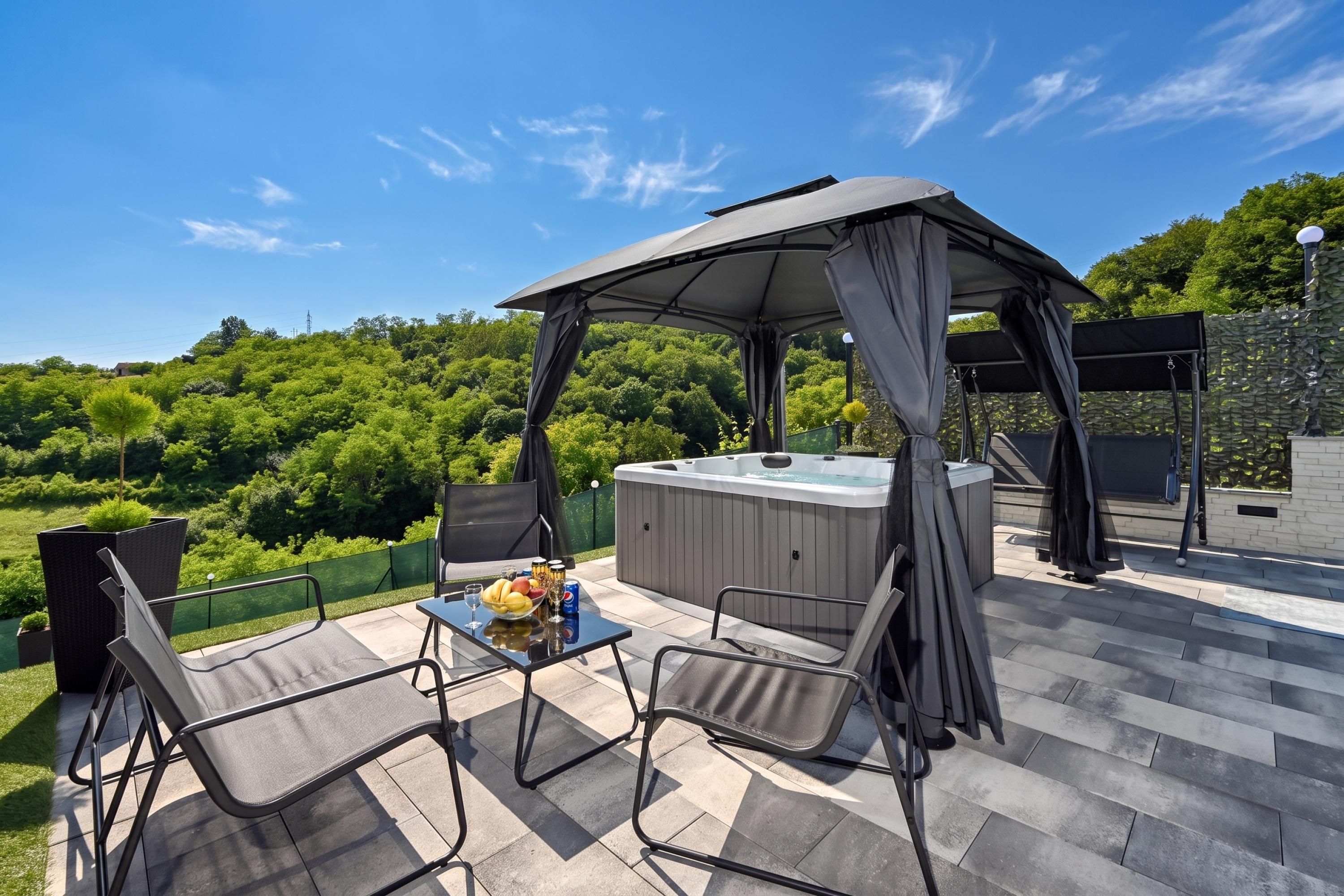An outdoor patio with a hot tub, a table with drinks, and two chairs.