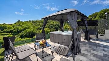 An outdoor patio with a hot tub, a table with drinks, and two chairs.
