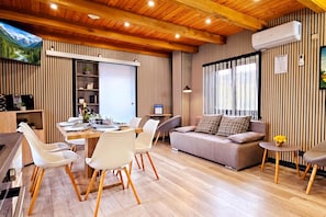 Una sala moderna con comedor, piso de madera y un ventanal con cortinas.