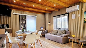 A modern living room with a wooden ceiling, a dining area with white chairs, a grey sofa, and a small side table with flowers. - AquaHaven With Private Pool And Wellness (Veliko Trgovisce)