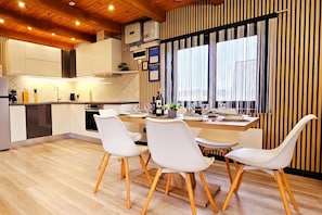 Una cocina moderna con armarios blancos, suelo de madera y un comedor con sillas blancas y una mesa de madera.