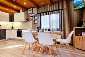 A modern kitchen with white cabinets, wooden flooring, and a dining area with white chairs. - AquaHaven With Private Pool And Wellness (Veliko Trgovisce)