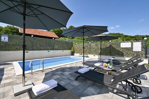 An outdoor swimming pool with lounge chairs and umbrellas, surrounded by a stone wall and greenery. - AquaHaven With Private Pool And Wellness (Veliko Trgovisce)