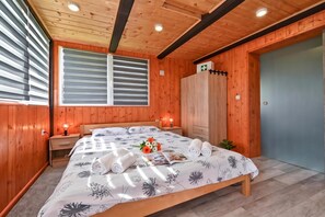 Una habitación con paneles de madera, una cama, lámparas de noche, un ventanal con persianas, un armario de madera y una puerta con un letrero verde.