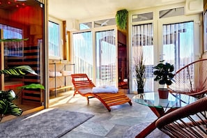 Un espacio interior moderno con una mesa de vidrio, un sillón de madera y plantas en macetas.