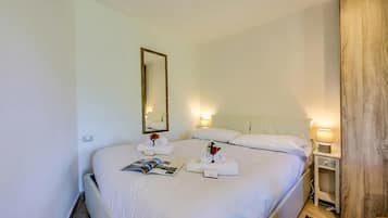 A neatly made bed with white linens, a bedside table with a lamp, and a mirror on the wall.