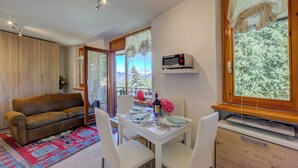 A living room with a sofa, dining table, chairs, a rug, and a view of trees through the window. - Studio La Borracina Mountain View (Sauze d'Oulx)