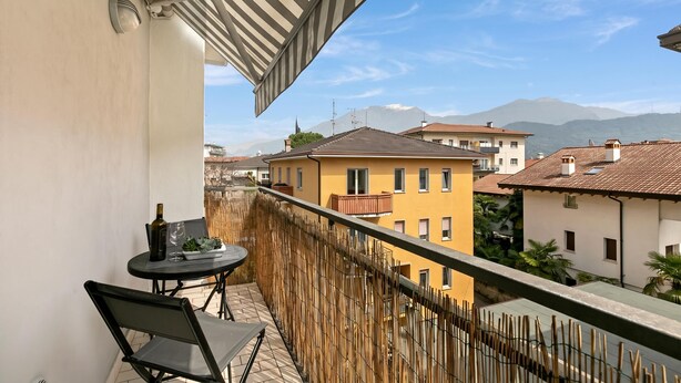 A balcony with a table and chairs, a bottle, and a glass, overlooking a residential area with buildings and mountains.