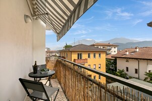 A balcony with a table and chairs, a bottle, and a glass, overlooking a residential area with buildings and mountains.