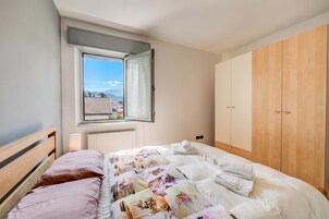 A bedroom with a bed, a window, a radiator, and wooden wardrobe.
