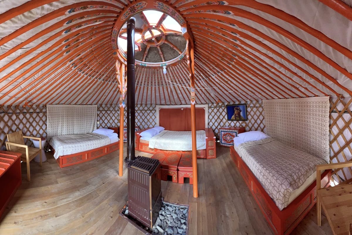 A traditional yurt with two beds, a central wooden structure, and a wooden floor.