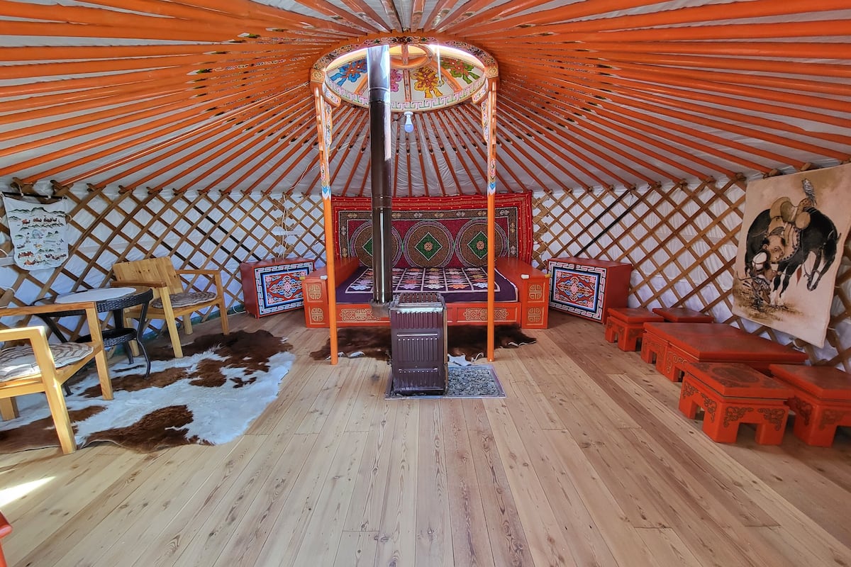 A yurt interior with a central bed, wooden furniture, and a decorative wall hanging.