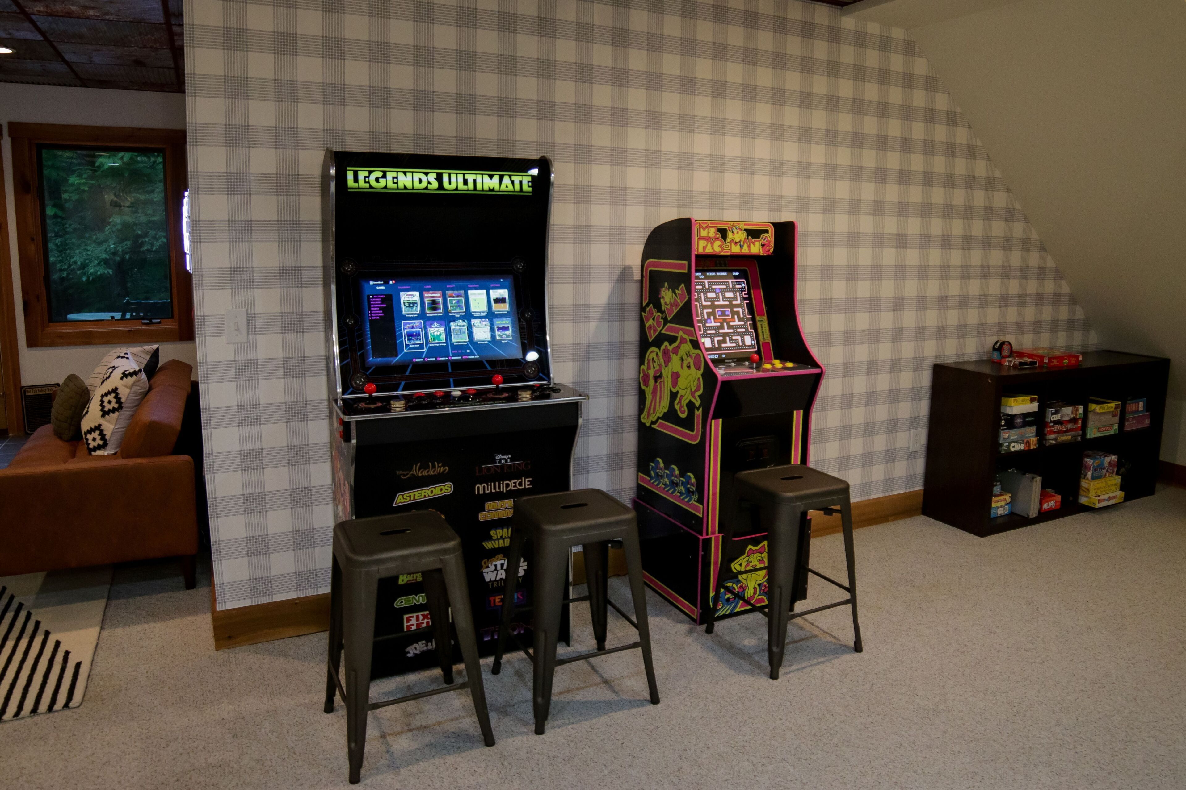 Une pièce avec deux bornes d’arcade, un canapé et une bibliothèque.