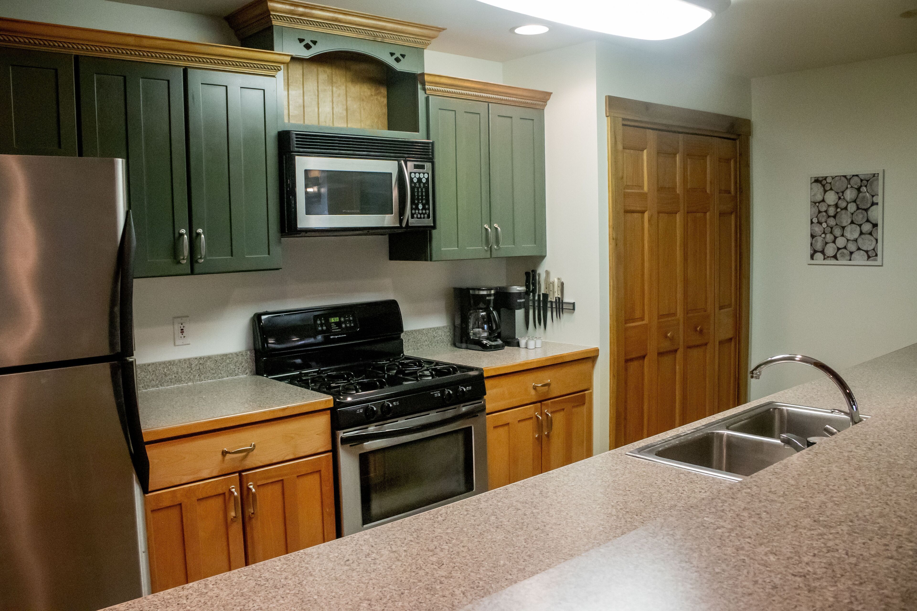 A kitchen with green cabinets, a stainless steel refrigerator, a microwave, a stove, and a sink.