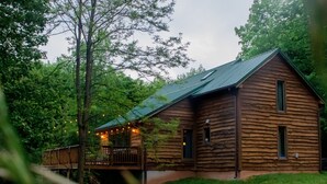 Een vakantiehuisje van hout met een houten terras en een kleine veranda, omringd door weelderige begroeiing.