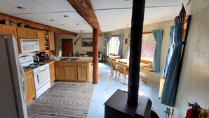 A kitchen with wooden cabinets, a stove, and a microwave. There is a dining area with a table and chairs. - Charming house with orchard and pond close to Flathead Lake (Rollins)
