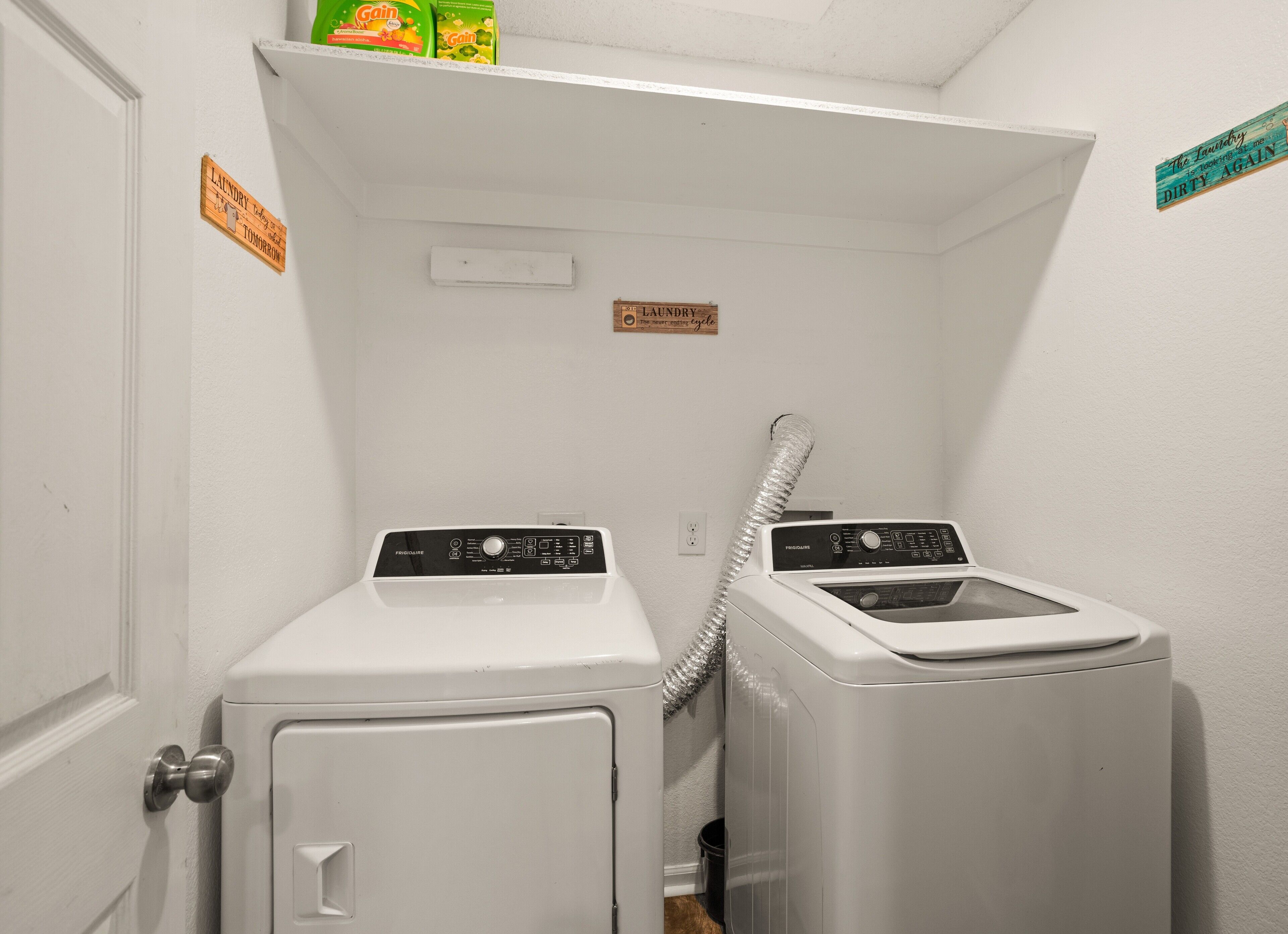 A laundry room with two front-loading washing machines and a dryer. There are signs on the wall indicating laundry instructions.