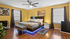 A bedroom with a bed, a nightstand, a desk, a chair, a ceiling fan, and a plant. - Beautiful Luxury Budget Home With Pool. Near 6Flags / AT&T (Grand Prairie)