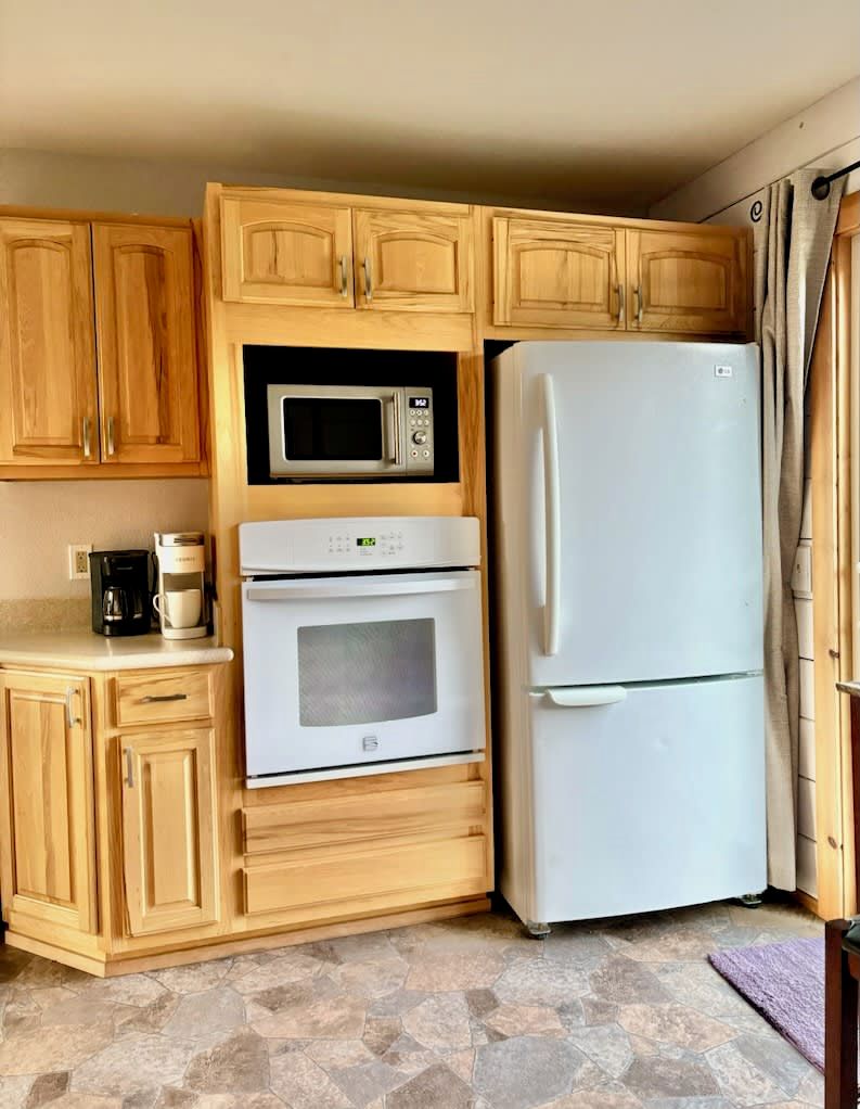 A compact kitchen with wooden cabinets, a microwave, a refrigerator, and an oven.