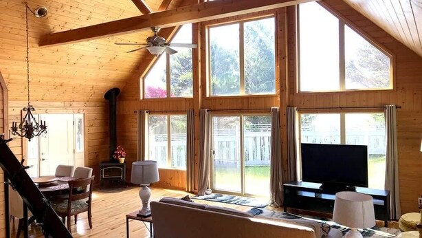 A spacious living room with large windows, a ceiling fan, a fireplace, and a television.