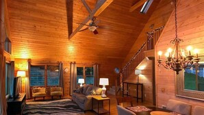 A cozy log cabin interior with a wooden ceiling, a staircase, a chandelier, and a sofa.