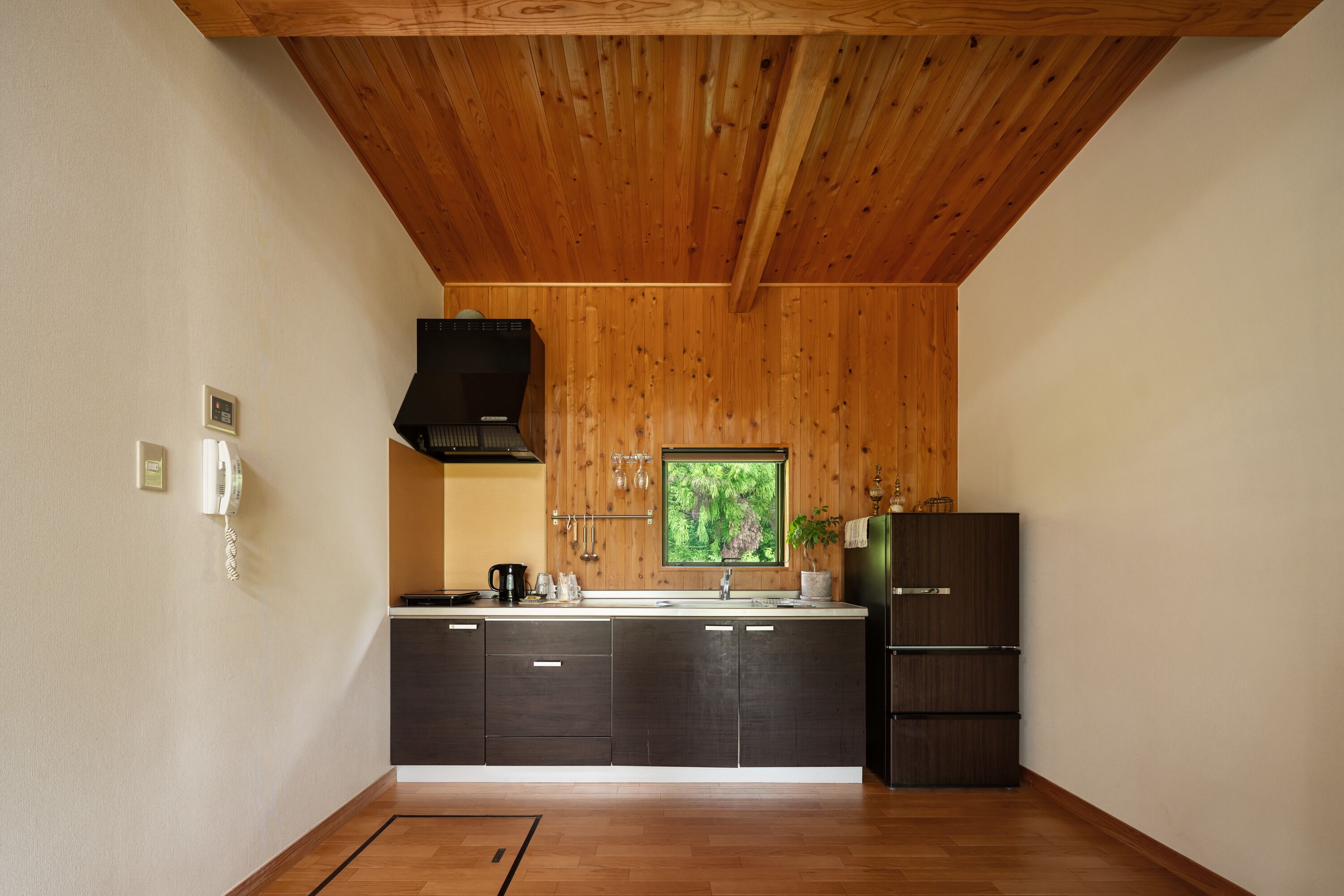 Een moderne keuken met houten balken in het plafond, een inbouwfornuis en een groot raam met uitzicht op groen.