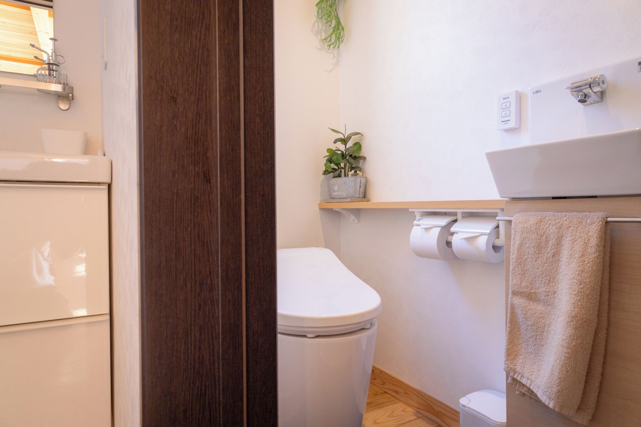 A bathroom with a toilet, a sink, a towel rack, and a small shelf with a plant.