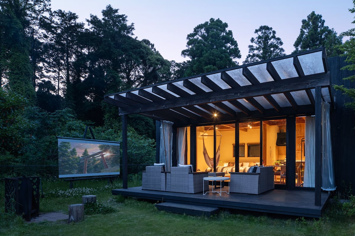 Un espacio exterior moderno con porche cubierto, zona de comedor y vistas al bosque circundante.