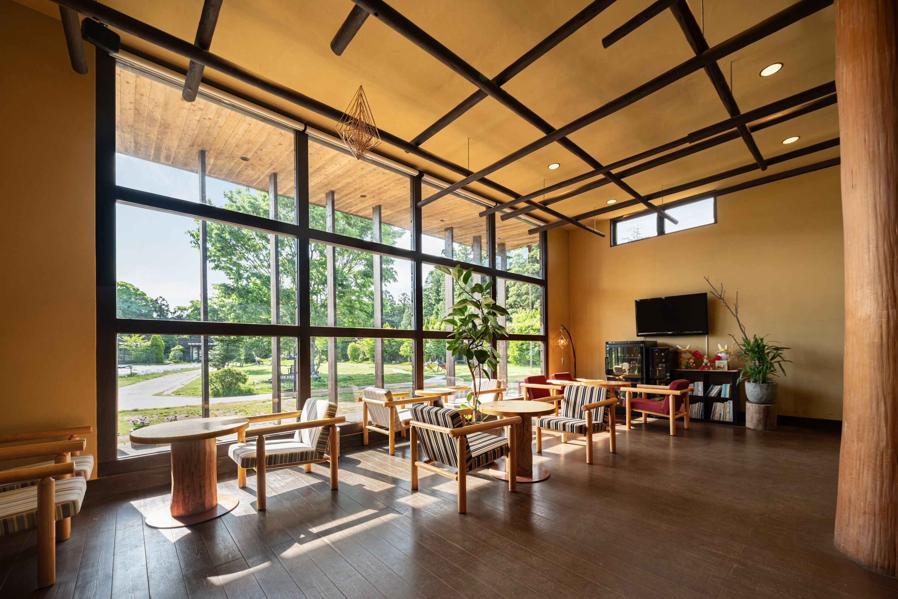 Una habitación amplia con grandes ventanales, muebles de madera y un televisor en la pared.