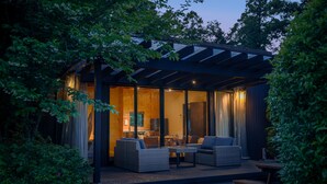 A modern outdoor living area with a wooden deck, wicker furniture, and a glass enclosure.