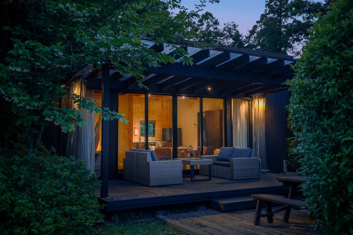 Un espacio moderno para disfrutar del aire libre con piso de madera, mobiliario de mimbre y cerramiento de vidrio.