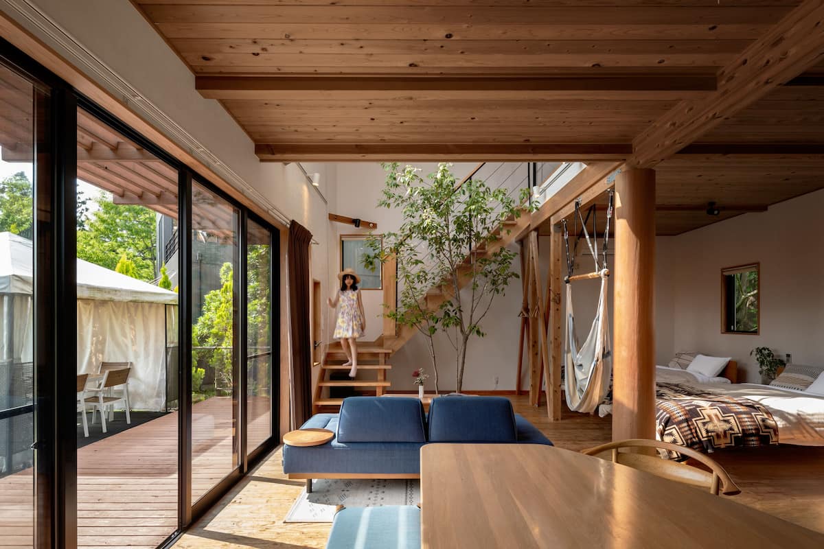 Un interior moderno con techo de madera, un sofá, una cama y una escalera que lleva a un espacio exterior.