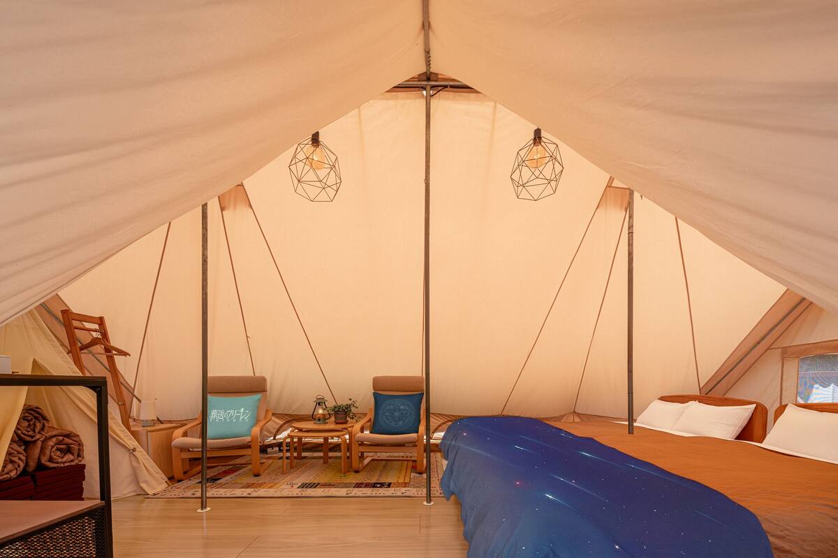 Una carpa con una cama, dos sillas, una mesa y luces colgantes.