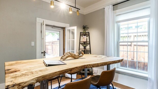 A dining area with a wooden table, two chairs, a vase, and a bookshelf.