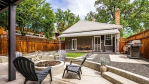 A backyard with a patio, outdoor seating, a barbecue grill, and a small garden area.