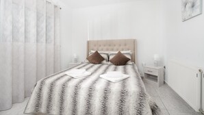 A bedroom with a bed, two pillows, a nightstand, a lamp, and a radiator. - MTC-Sea & sky by Valeria near airport (Markopoulo Mesogaias)