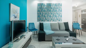 A modern living room with a flat-screen TV, a sofa, two chairs, a coffee table, and a large floral artwork on the wall. - MTC-Sea & sky by Valeria near airport (Markopoulo Mesogaias)
