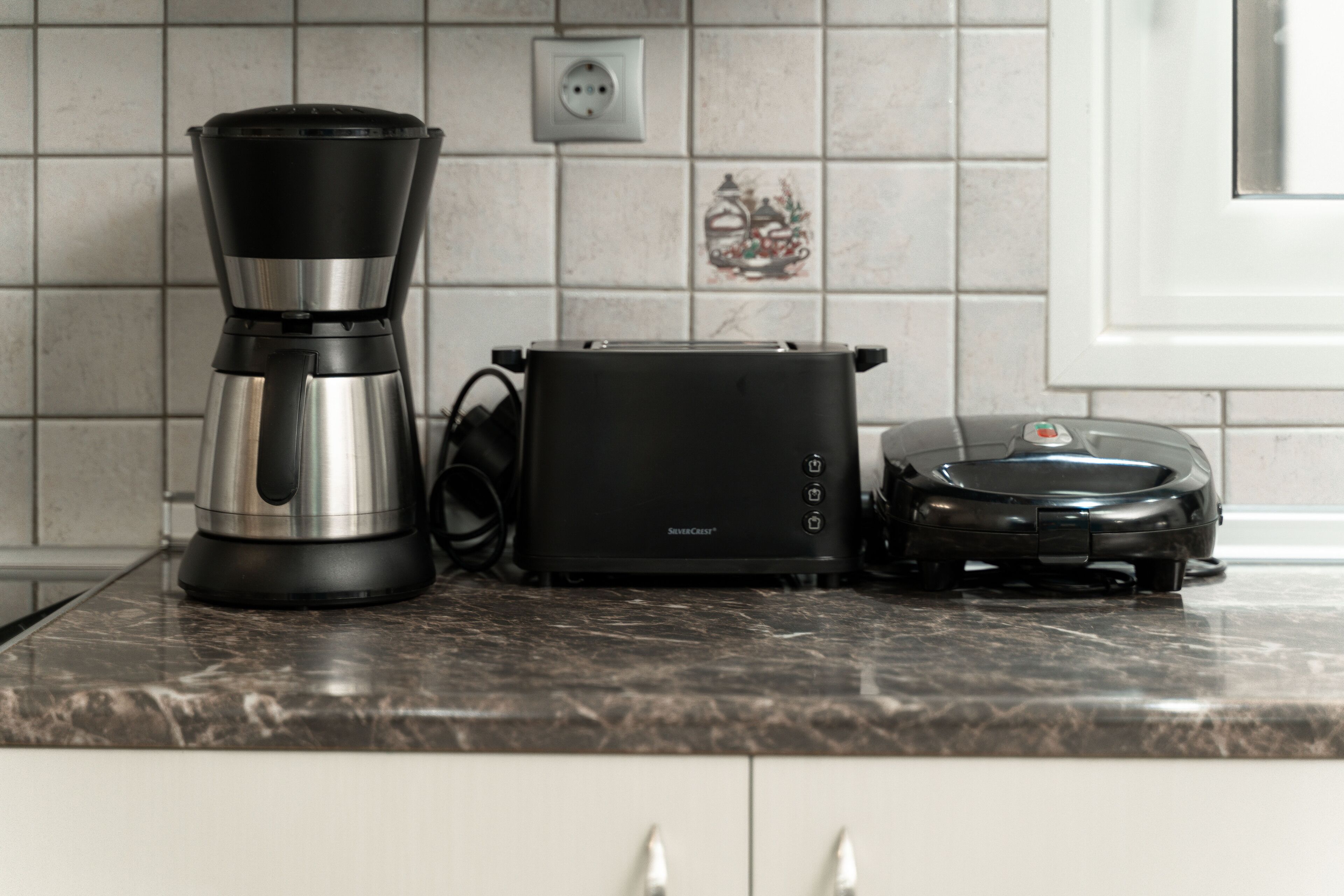 Una encimera de cocina con cafetera, tostadora y robot aspirador.