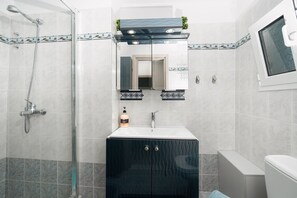 Et badeværelse med bruseniche i glas, en hvid vask, mørke skabe og et toilet.