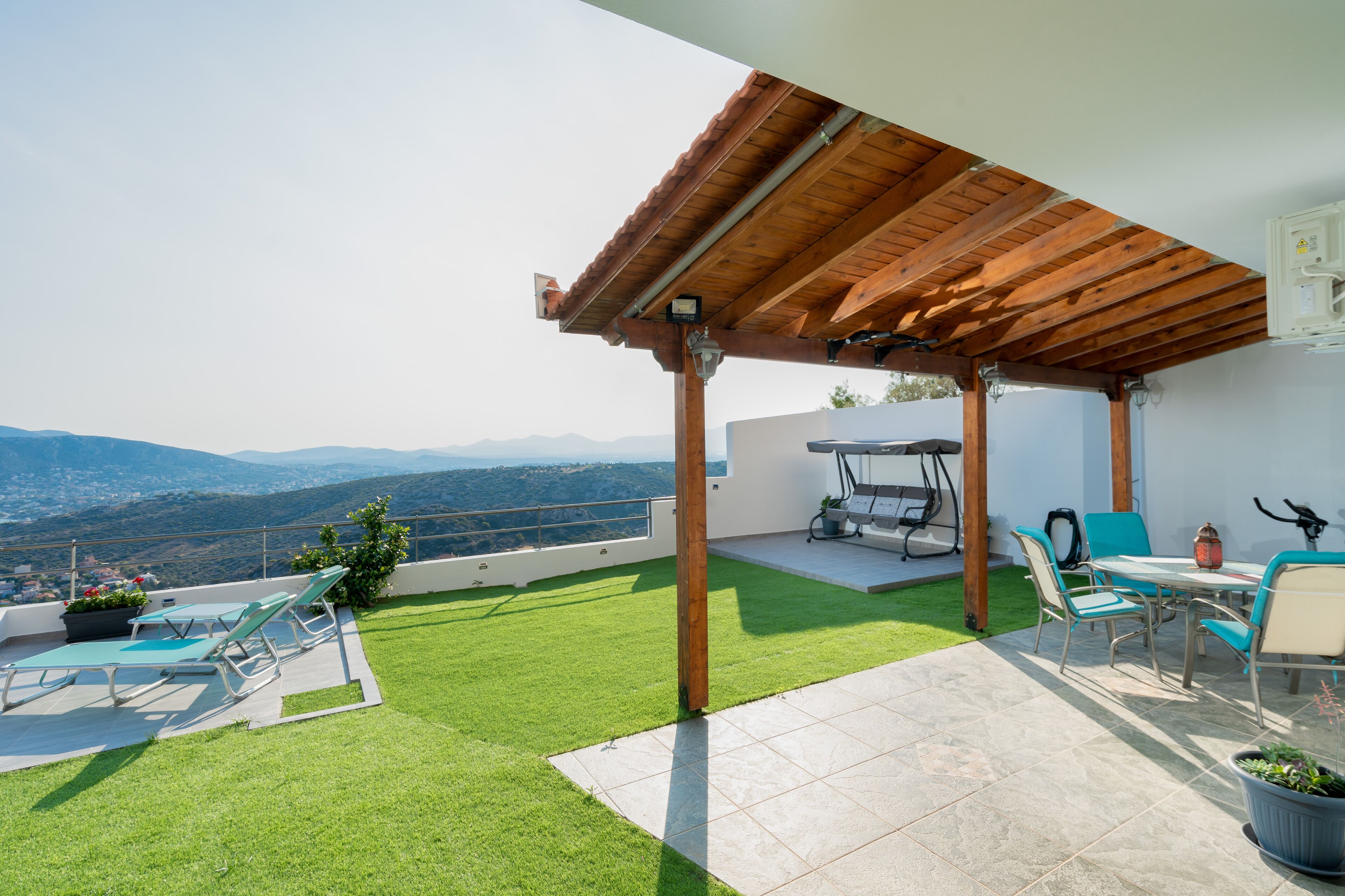 Eine Dachterrasse mit einer Holz-Pergola, einem Essbereich mit Stühlen und einem Tisch sowie Blick auf die Berge.