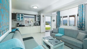 A modern living room with a grey sofa, a coffee table, and a view of the outdoors through a large window. - MTC-Sea & sky by Valeria near airport (Markopoulo Mesogaias)