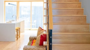 Ein modernes Interieur mit einer Holztreppe, einer Küchenzeile und einer Sitzecke mit Kissen.