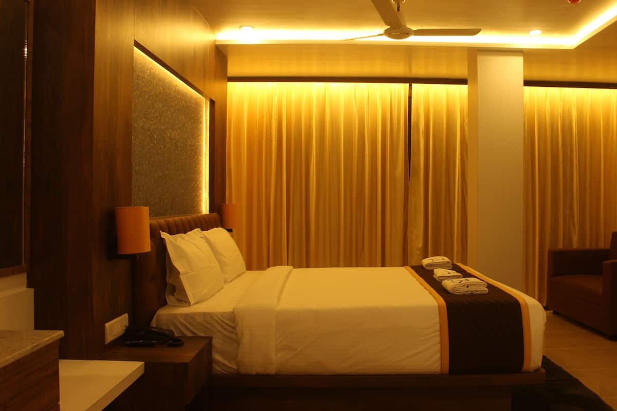 A hotel room with a large bed, a bedside table, a chair, a lamp, and curtains.