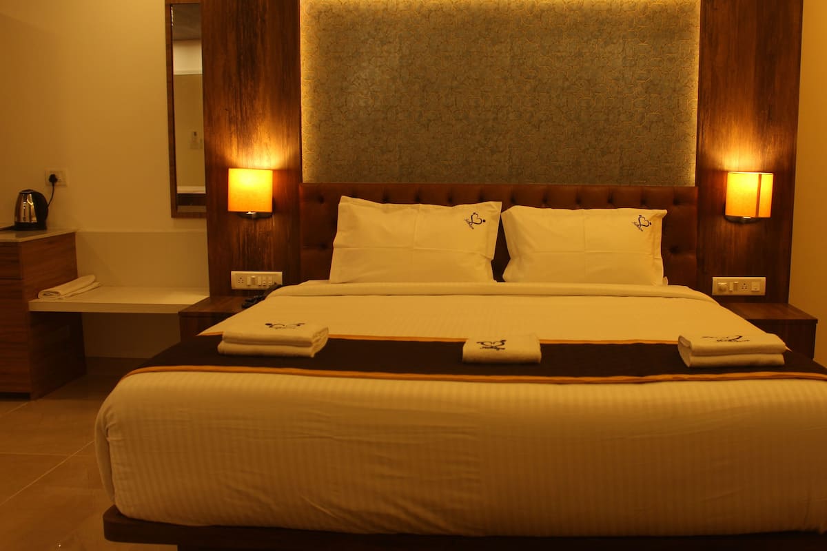 A hotel room with a large bed, two bedside lamps, a wooden headboard, and a small bedside table with a lamp.