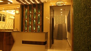 Una zona de recepción con un mostrador de madera, una pared con paneles de vidrio verticales y una escalera que sube a otro piso.