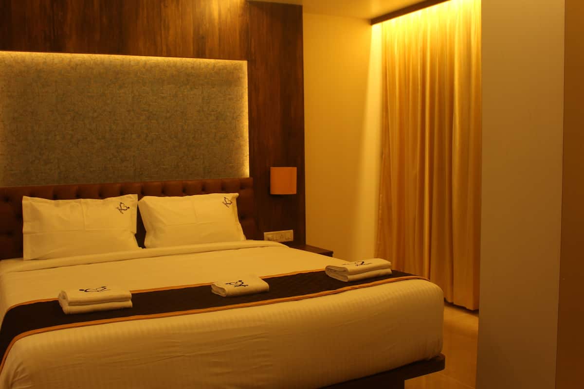 A hotel room with a large bed, a headboard with a textured panel, two bedside lamps, and a window with curtains.