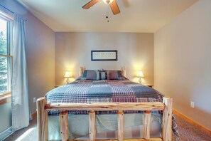 Une chambre à coucher avec un lit, deux lampes de chevet, un ventilateur de plafond et une fenêtre avec des rideaux.