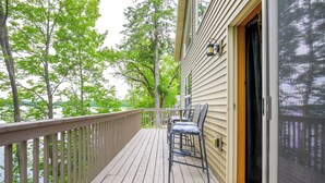 Une terrasse en bois avec des chaises, une rambarde et une vue sur des arbres et un bâtiment.